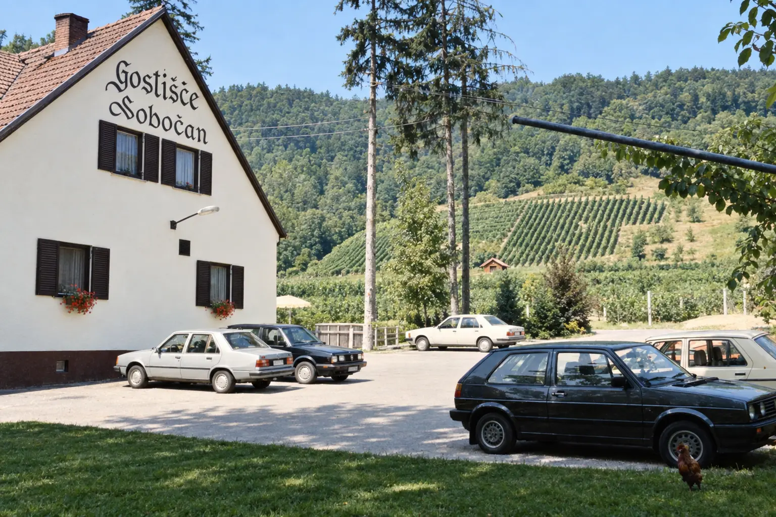 Gostišče Sobočan s parkiriščem pred poslopjem, v ozadju gozdnati griči in vinograd